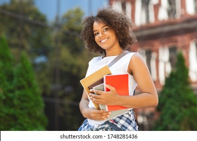 Student Orientation Concept. Portrait Of Happy Black Teen Girl With Backpack And Workbooks Standing Outdoors In College Campus, Posing To Camera