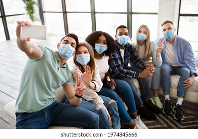 Student Party During Coronavirus Epidemic. Group Of Fun Multiethnic Friends In Face Masks Taking Selfie With Smartphone On Social Gathering At Home, Wearing Protection Against Virus