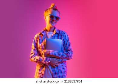 Student. Portrait Of Adorable Young Girl Wearing Plaid Shirt Using Tablet Isolated On Magenta Color Background In Neon Light. Concept Of Beauty, Art, Fashion, Youth, Sales And Ad, Education, Studying.