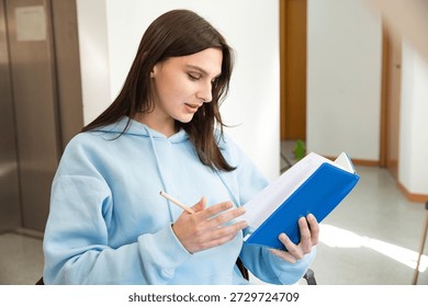 student preparing for study with notebook. A beautiful girl in a blue sweatshirt holding a notebook