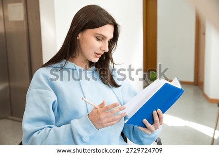 student preparing for study with notebook. A beautiful girl in a blue sweatshirt holding a notebook