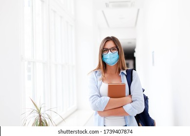 Student In Protective Face Mask In Empty College Indoors. Young Woman Going To Exams In High School. Girl With Backpack And Book In University Corridor. Social Distancing During Quarantine.