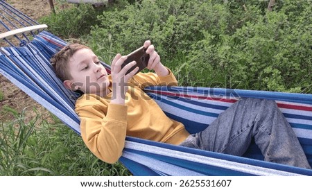 Student resting during summer holidays, boy lying in hammock and looking at smartphone, online learning, outdoor recreation during summer holidays