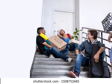 Student Roommates Sitting On Staircase Tired Of Moving To New Flat In College Campus.Friends Waiting In Front Of The Door To Go On Travel Together On Holiday 