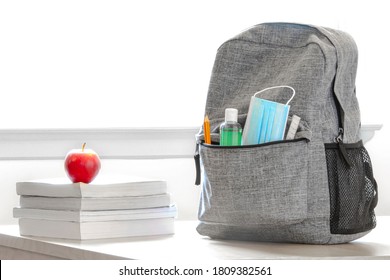 Student school bag pack with sanitizer, a face mask, pencils, books and an apple on a table. Back to school during global pandemic. Covid 19.