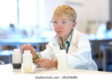 Student, School Boy, In Safety Glasses And White Lab Coat Making Experiments In The Chemical Laboratory