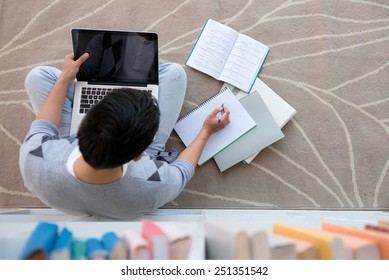 Student Sitting On The Floor With A Laptop And Doing Homework, View From Above