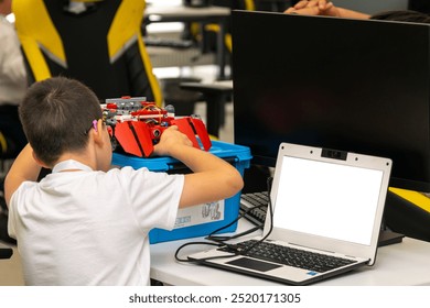 A student sitting at a table assembles and programs a robot via a netbook