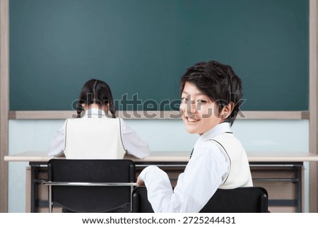 Student smiles at the camera while classmate focuses on work in classroom setting