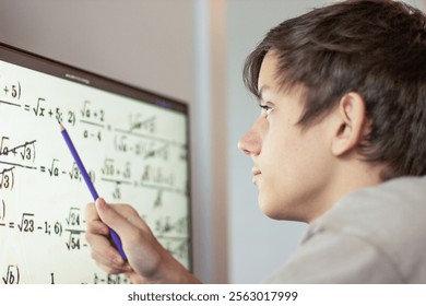 A student solves math problems on a computer. a teenage boy is studying online