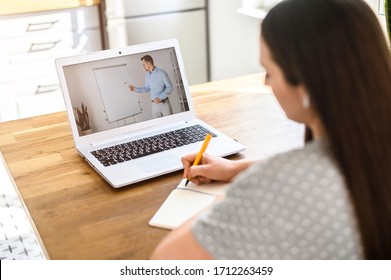 A student studies online. A student girl is watching online classes and writing a syllabus in notebook. Concept of distance study, online learning, webinars. Back view