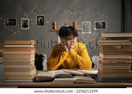 Student studying hard exam with books, tired guy read difficult book in dormitory. Copy space