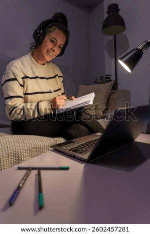 Student studying remotely, typing notes with laptop and headphones during late night virtual learning session