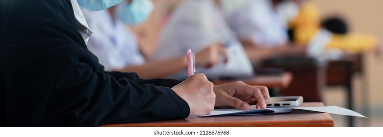 Student Taking Exam While Wearing Face Mask Due To Coronavirus Emergency. Young Woman Sitting In Class With Wearing Surgical Mask Due To Covid-19 Pandemic