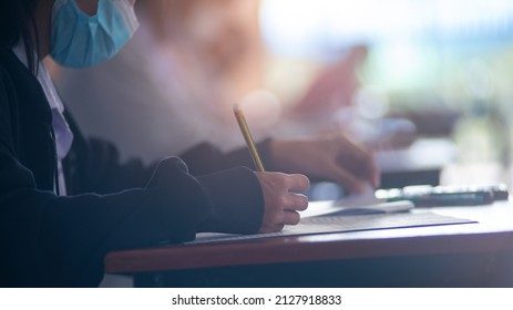 Student Taking Exam While Wearing Face Mask Due To Coronavirus Emergency. Young Woman Sitting In Class With Wearing Surgical Mask Due To Covid-19 Pandemic