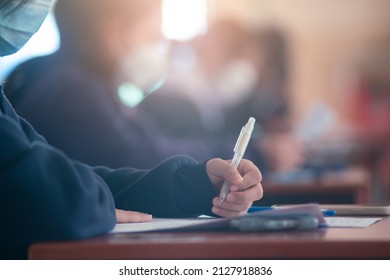 Student Taking Exam While Wearing Face Mask Due To Coronavirus Emergency. Young Woman Sitting In Class With Wearing Surgical Mask Due To Covid-19 Pandemic