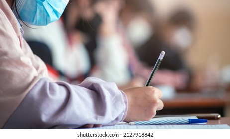 Student Taking Exam While Wearing Face Mask Due To Coronavirus Emergency. Young Woman Sitting In Class With Wearing Surgical Mask Due To Covid-19 Pandemic