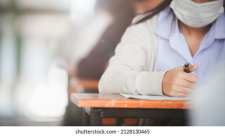 Student Taking Exam While Wearing Face Mask Due To Coronavirus Emergency. Young Woman Sitting In Class With Wearing Surgical Mask Due To Covid-19 Pandemic