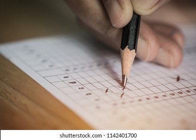 Student taking exams, writing examination on paper answer sheet optical form of standardized test on desk doing final exam in classroom, Examination sitting on row chair in school.