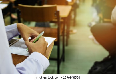 Student Taking Test For Final Assessment In The Classroom; Education Concept Image Of Learner On A Desk Holding A Pen To Do Class Assignment In The Lecture Room Or At The Training And Learning Center 