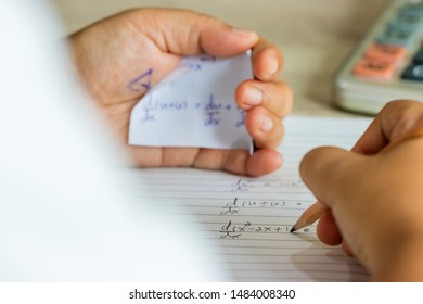 Student using formula math sheet to cheat on test. Hand of university student holding pencil doing math question in examination and cheating with answer piece of paper in hand. Education concept.