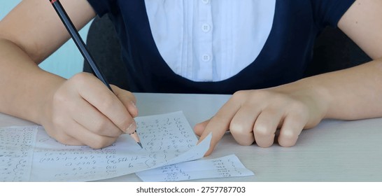Student using formula math sheet to cheat on test. Hand of university student holding pencil doing math question in examination and cheating in test with answer piece of paper in hand.