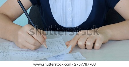 Student using formula math sheet to cheat on test. Hand of university student holding pencil doing math question in examination and cheating in test with answer piece of paper in hand.