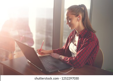 Student Using Online Education Service. Young Woman Looking In Laptop Display Watching Training Foreign Language Courses And Taking Notes In Notebook. Modern Study Technology Concept. 