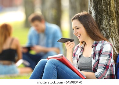 Student Using Voice Recognition With A Smart Phone To Record Notes Sitting On The Grass In A Park