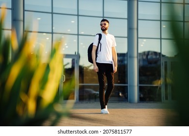 A Student Walking Around The City With A Backpack And A Laptop. Attractive Young Man In Sunglasses Walks Down The Street On A Sunny Day, Education Concept