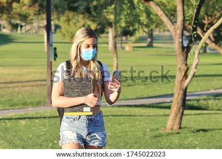 A student wearing a mask walking on campus looking at her phone.