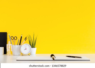 Student workplace. Desk with school stationery, clock against yellow wall mockup. 