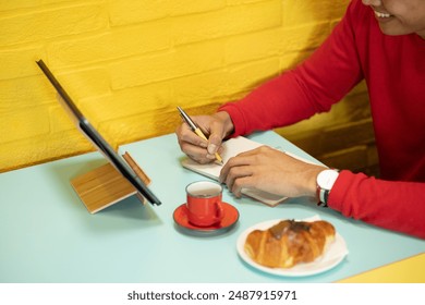 Student is writing in a notebook while enjoying a coffee break with a croissant
