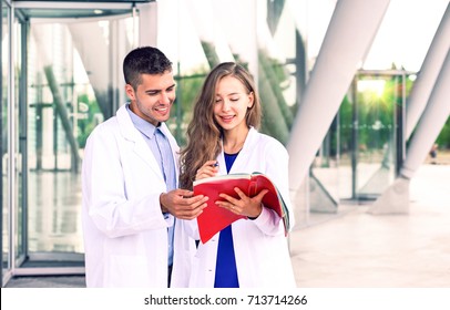 Student and young doctor helping with papers - Dentist and assistant nurse wearing medical white coat standing at modern hospital holding book - Concept of education and professional training - Shutterstock ID 713714266