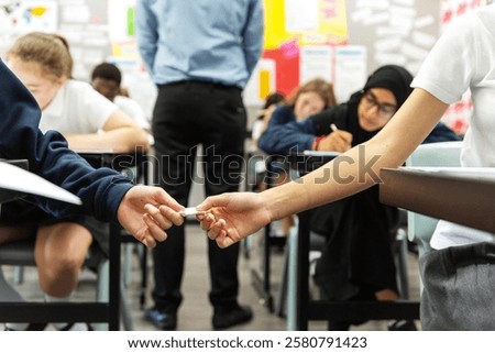 Students in a classroom taking a test. Focus on a hand passing a note. Diverse group, including a student in a hijab. Classroom, test, note passing. Students cheating on an exam by passing a note.