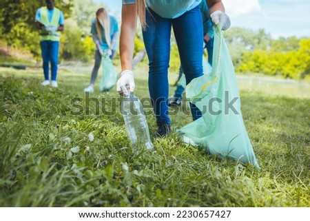 Students clean the local park, collect garbage in bags. On a beautiful sunny day, a group of young volunteers collect garbage in nature. Focus in foreground