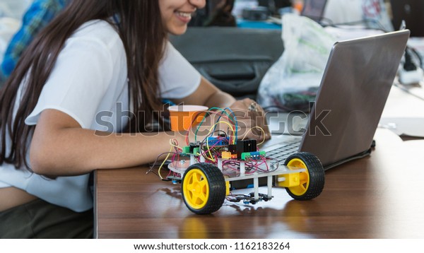 Students code\
a metal car robot and an electronic board. Robotics and\
electronics. Laboratory. Mathematics, engineering, science,\
technology, computer code. STEM education.\

