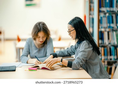 Students completing homework assignment at library table reading textbooks collaborative learning concept. Students preparing for exam at library desk reading textbooks focused revision academic concentration. 