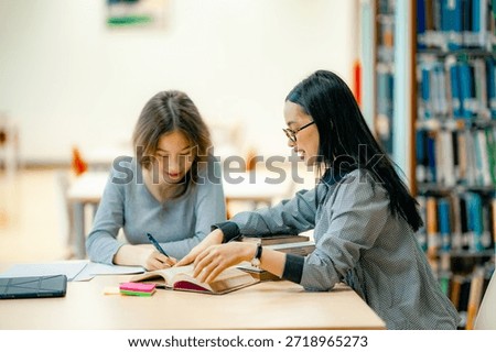 Students completing homework assignment at library table reading textbooks collaborative learning concept. Students preparing for exam at library desk reading textbooks focused revision academic concentration. 
