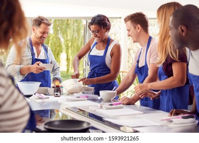 Students In Cookery Class Mixing Ingredients For Recipe In Kitchen