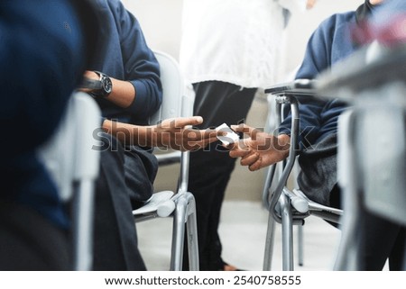Students discreetly passing notes in a classroom. Note passing among students, a common classroom scene. Engaged students exchanging notes during class. Cheating on exams.