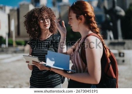 Students engage in a conversation while reviewing a written document in an outdoor school courtyard on a sunny day. They appear to be collaborating on an academic project or discussing their studies.