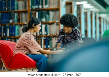 Students engaged in discussion using tablet in library showing peer learning academic support focused study routine higher education environment.
