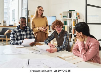 Students engaging in group study session reviewing foreign languages with materials and textbooks around large table. Instructor standing nearby, assisting and smiling