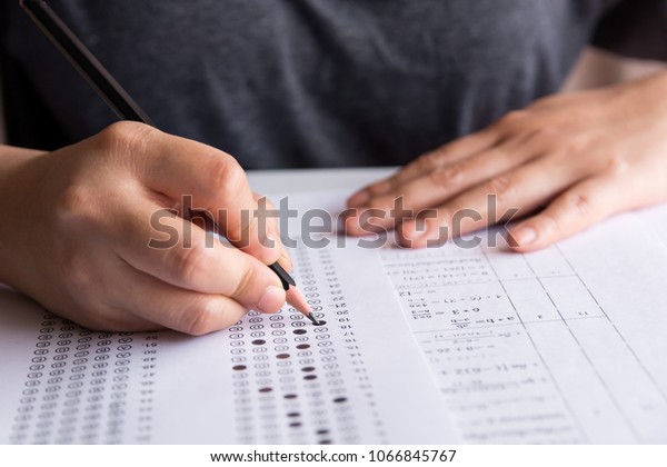 Students hand holding pencil writing\
selected choice on answer sheets and Mathematics question sheets.\
students testing doing examination. school exam\
