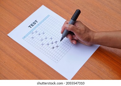 Student's Hand Holds Pen To Do The Test, Makes Cross Marks On Optical Form Or Multiple Choices Answer Of Paper Test On Table. Concept : Educational Evaluation. Examination.  Education School Test 