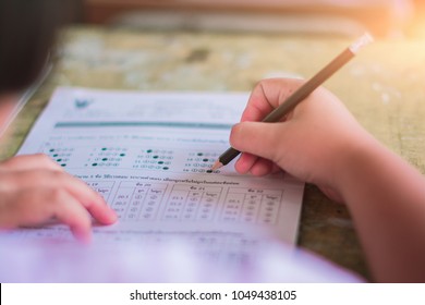 students hand testing doing examination with pencil drawing selected choice on answer sheets in classroom at school.