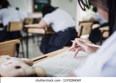 Students hand testing doing examination with pen drawing selected choice on answer sheets in school exams, blur pupils college backgroud. Education system tests concept.