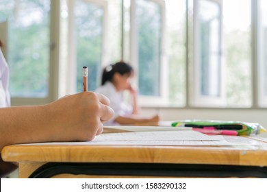 Students Hands Taking Exams, Writing Examination Room With Holding Pencil On Optical Form Of Standardized Test With Answers And English Paper Sheet On Row Desk Chair Doing Final Exam In Classroom.