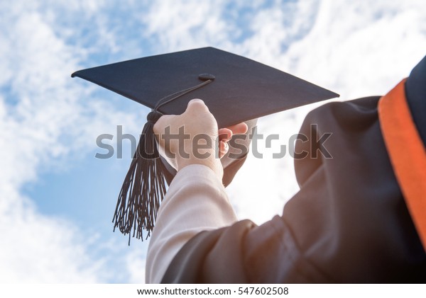 The students holding a shot of graduation cap by their\
hand in a bright sky during ceremony success graduates at the\
University, Concept of Successful Education in Hight\
School,Congratulated Degree\
